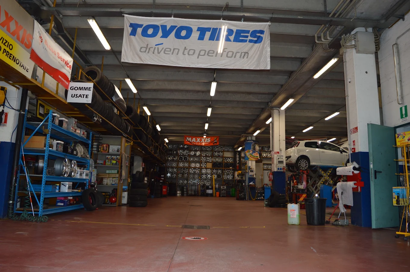 Interno dell'officina Autocar Service, con auto sul ponte sollevatore e magazzino cerchi e gomme